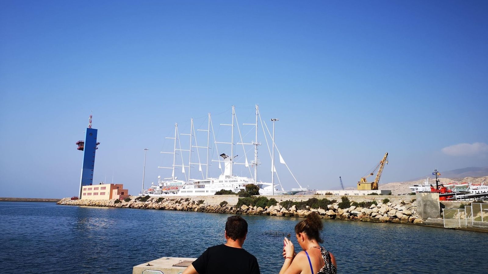 Una pareja fotografía desde el paseo marítimo las vistas del muelle con la torre de control y el edificio de la Autoridad Portuaria.