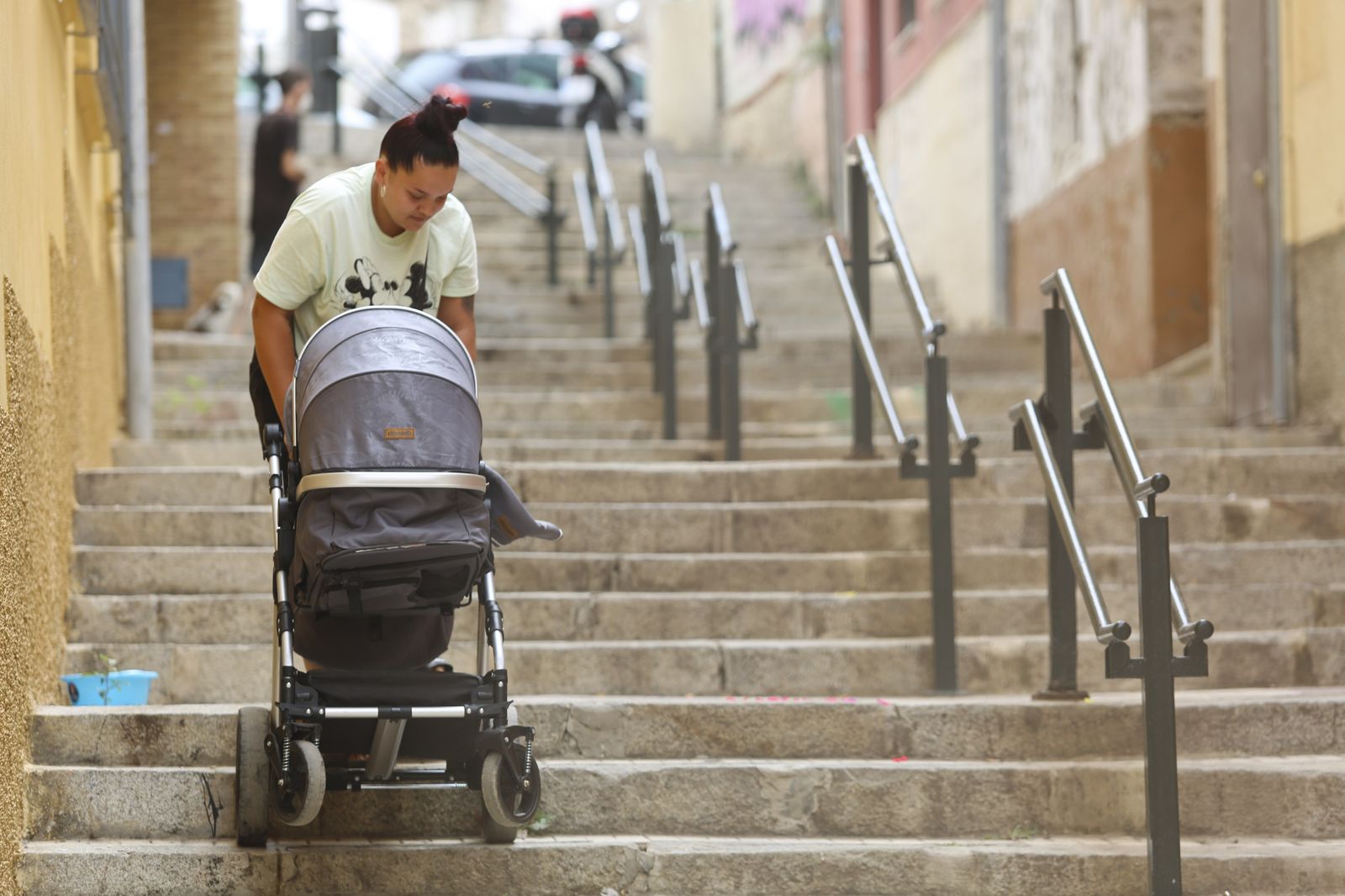 Una mujer sube el carrito de su hija por las escaleras