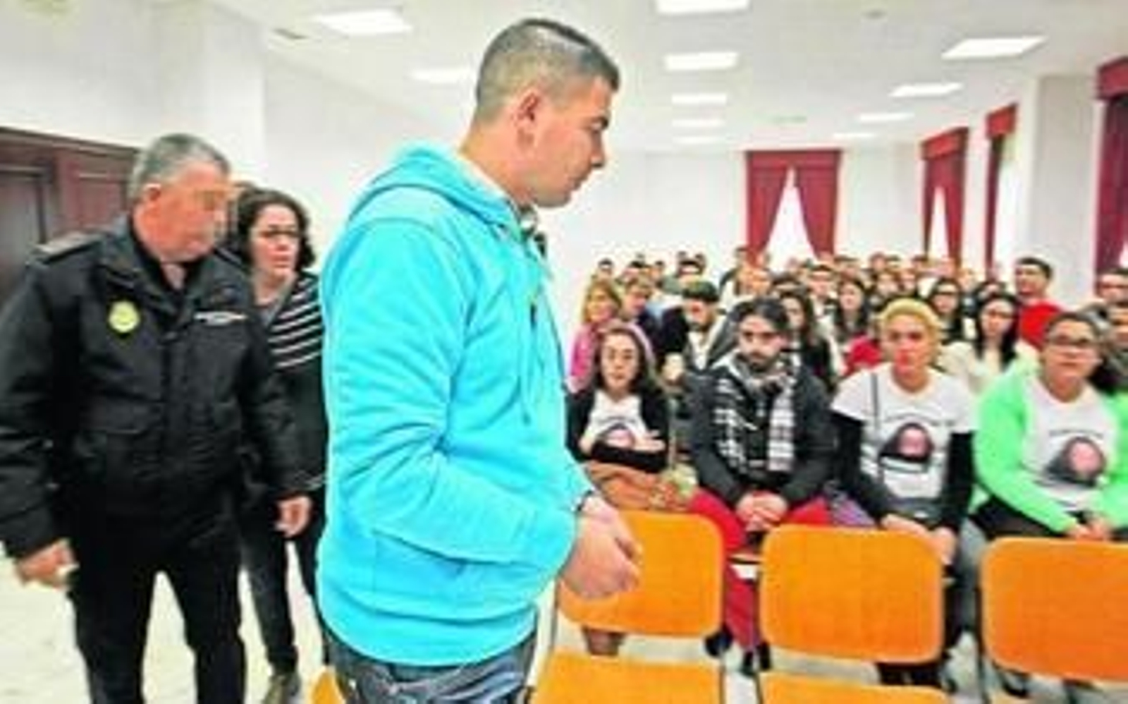 El acusado accede al banquillo, finalmente se sentó junto a su abogado, mientras amigos de la víctima portan su imagen en unas camisetas.