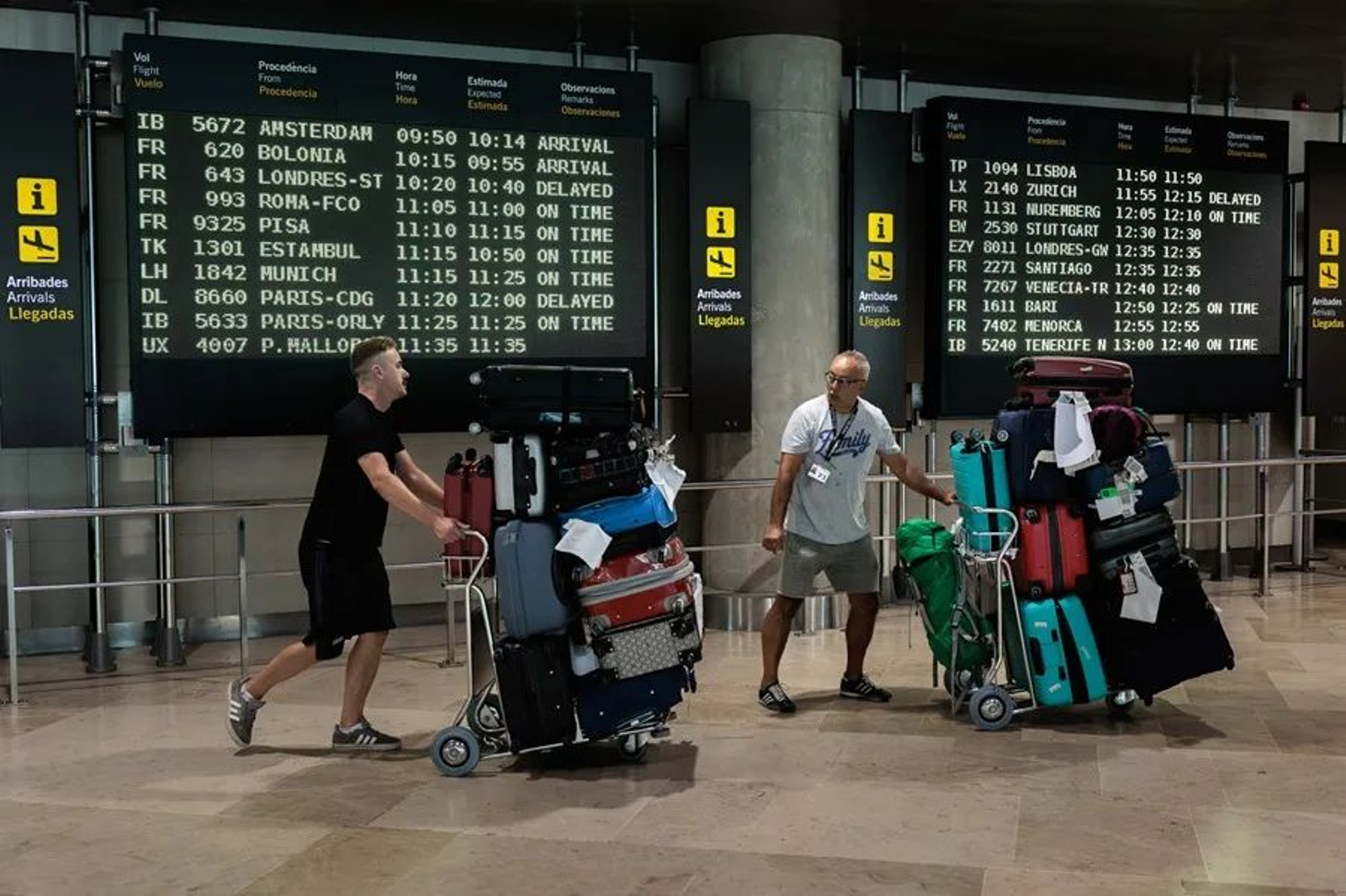 Dos personas transportan maletas en la zona de llegadas de un aeropuerto.