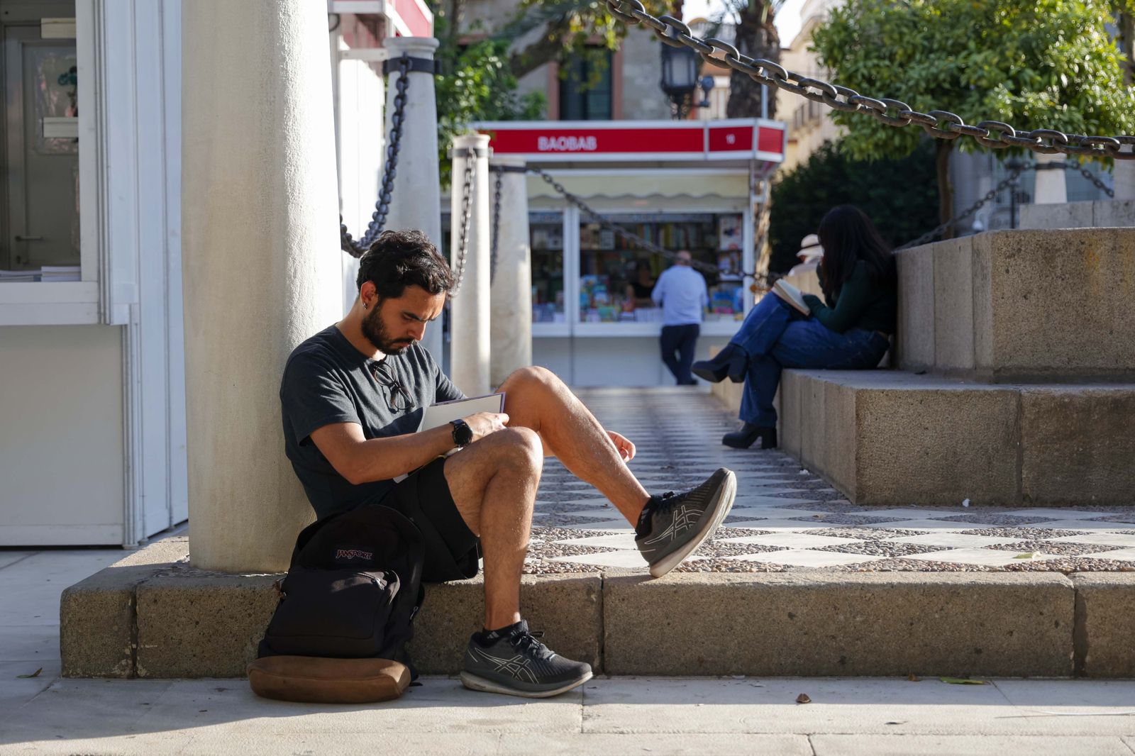 Un joven lee un libro en la Plaza Nueva, enclave principal de la Feria del Libro de Sevilla.