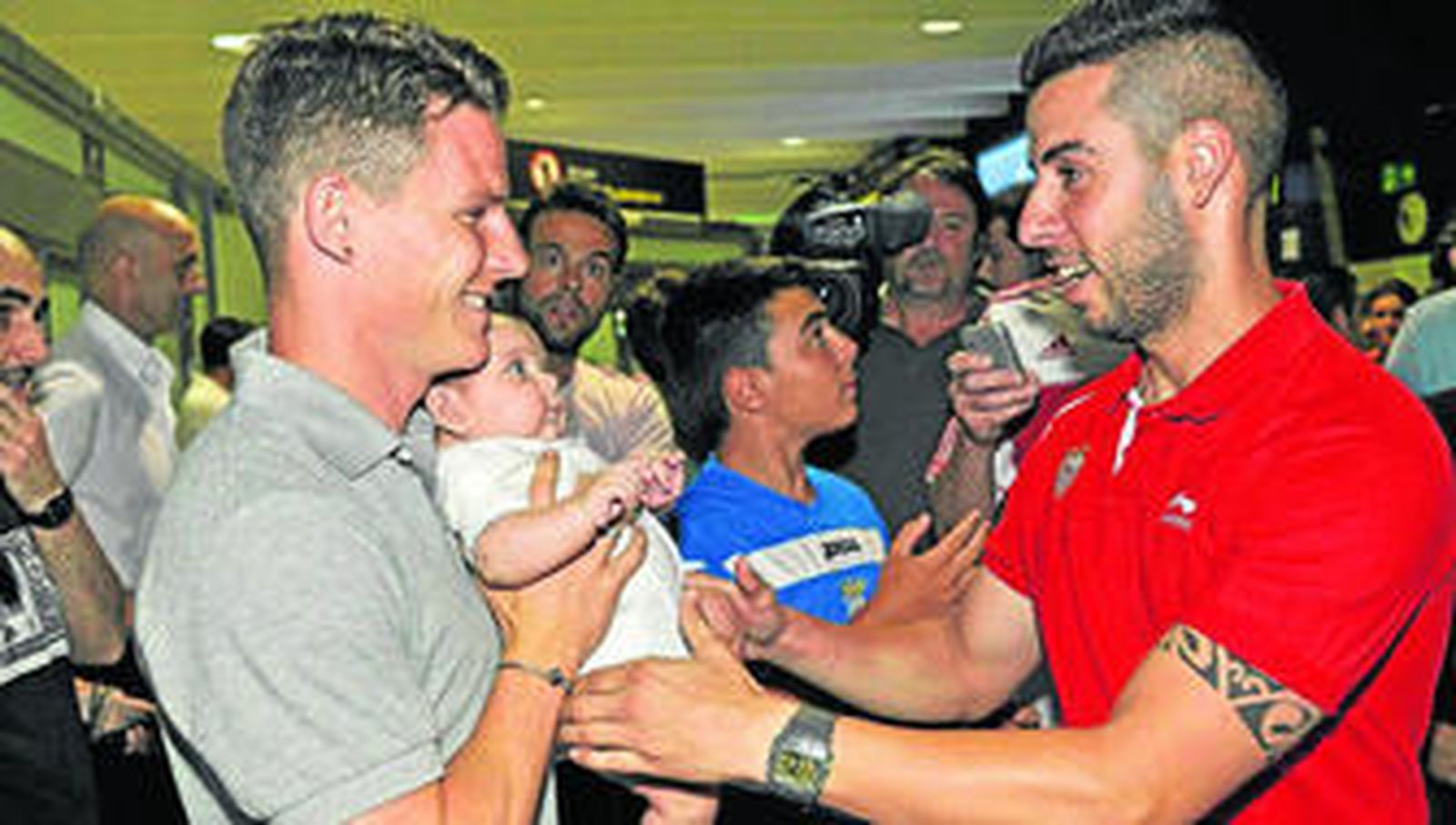 Gameiro sostiene el bebé de un joven a su llegada al aeropuerto de San Pablo, que registró una nutrida presencia de aficionados sevillistas.