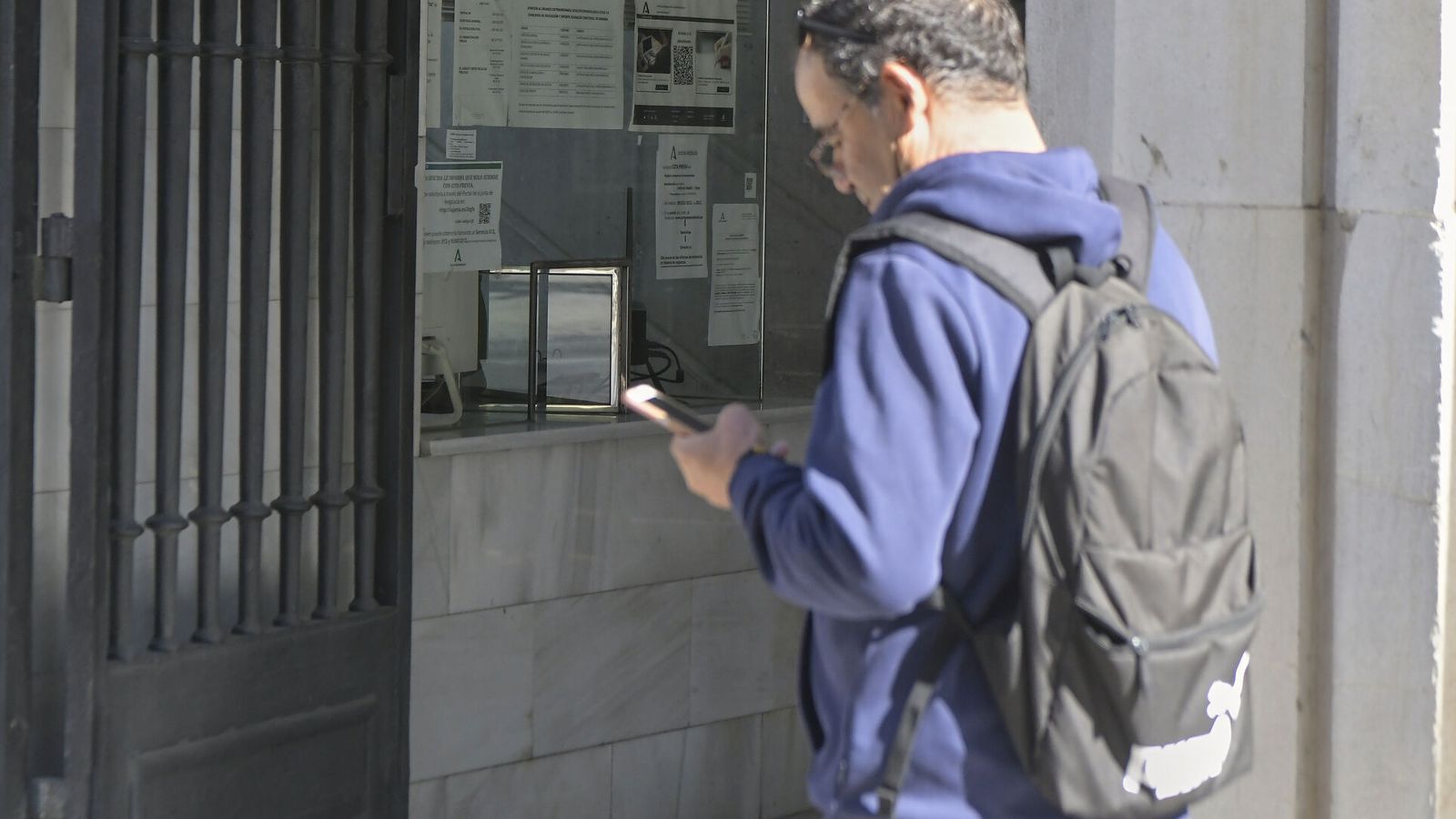 Un hombre comprueba su cita previa en el movil antes de entrar al edificio de La Normal