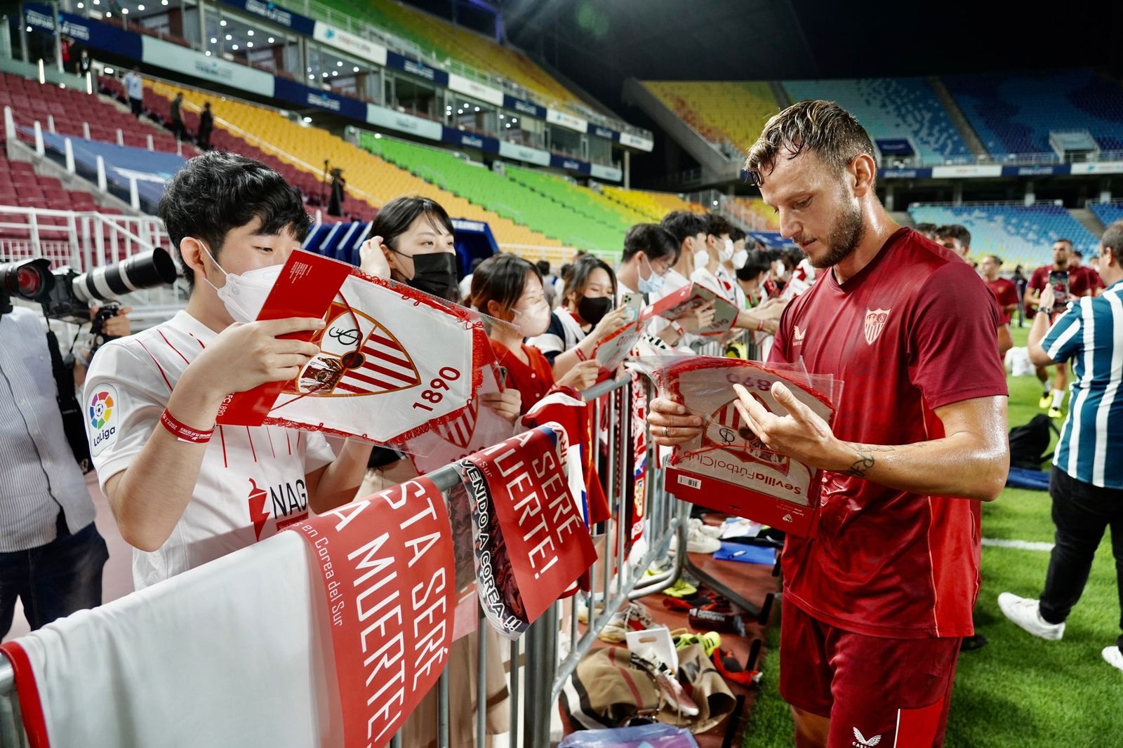 Rakitic, muy sudoroso en el húmedo ambiente coreano, reparte banderines a aficionados locales.