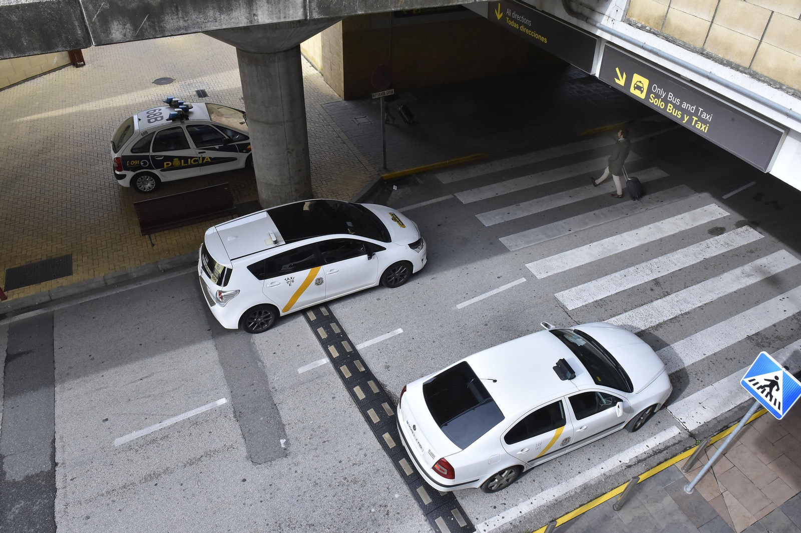 Dos taxis circulan por la terminal de llegadas del aeropuerto de San Pablo, mientras un patrullero de la Policía permanece aparcado cerca.