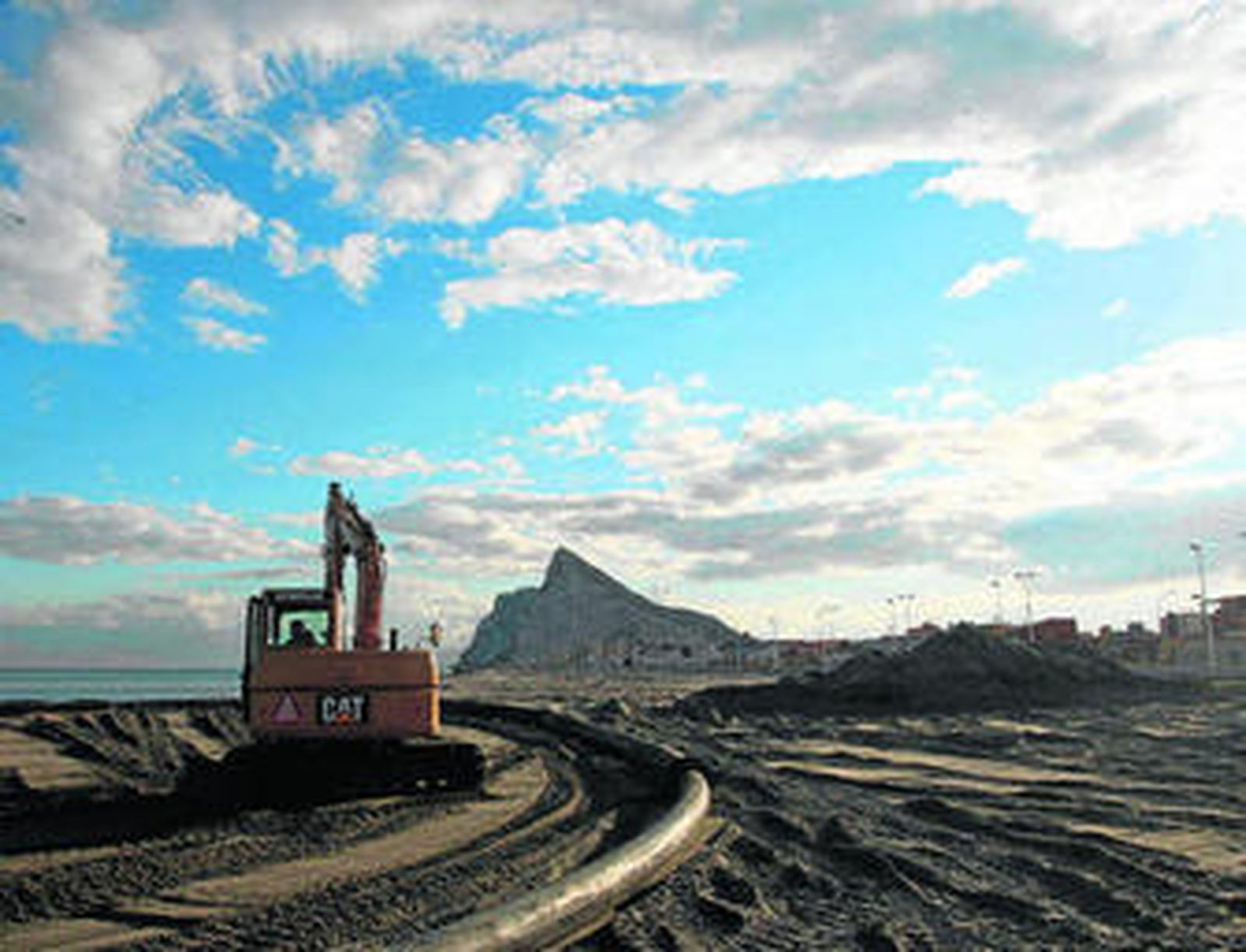 Una máquina extiende en la playa la arena dragada en el puerto de La Atunara.