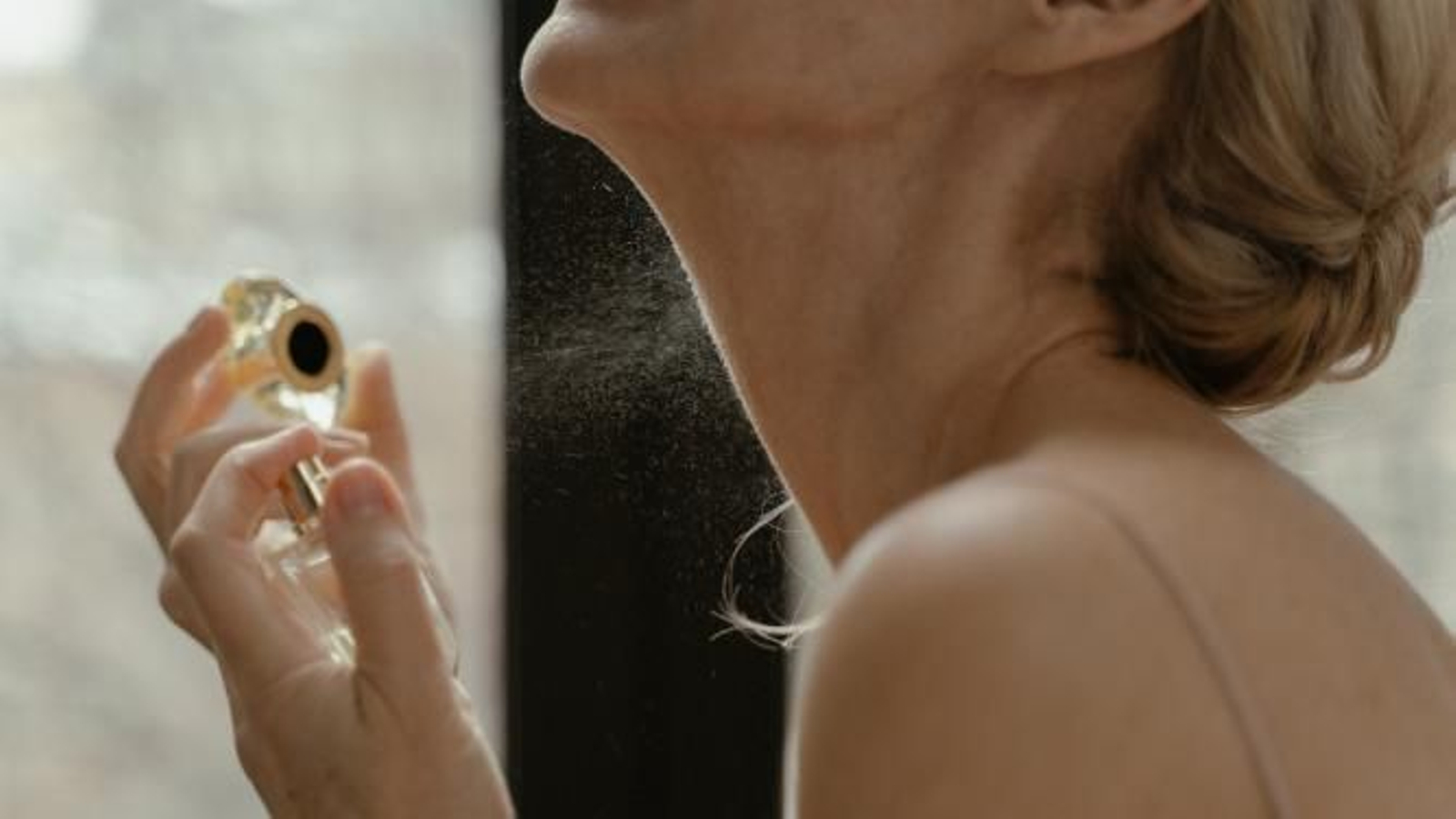 Mujer poniéndose perfume en el cuello.