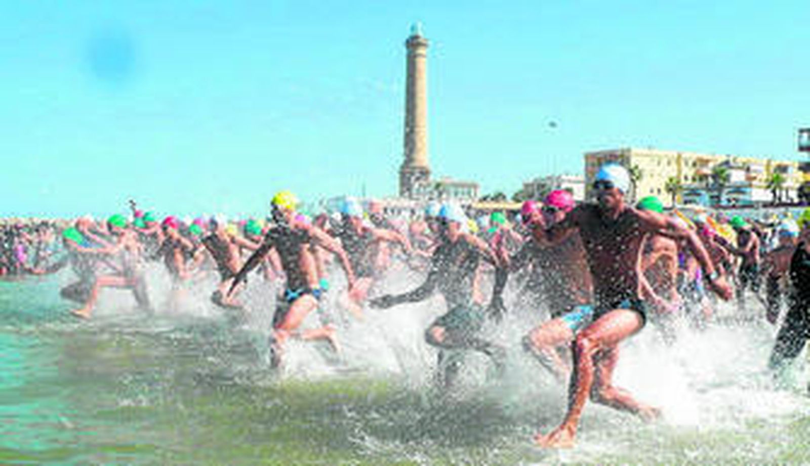 Los nadadores entran al agua, con el Faro de Chipiona al fondo.