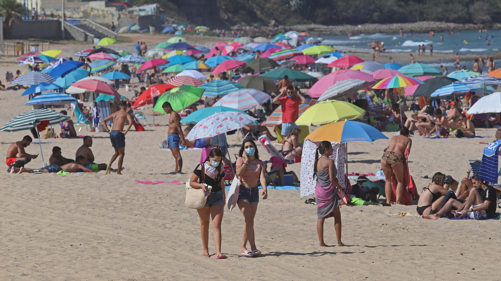 Un grupo de jóvenes camina por la playa con mascarillas.