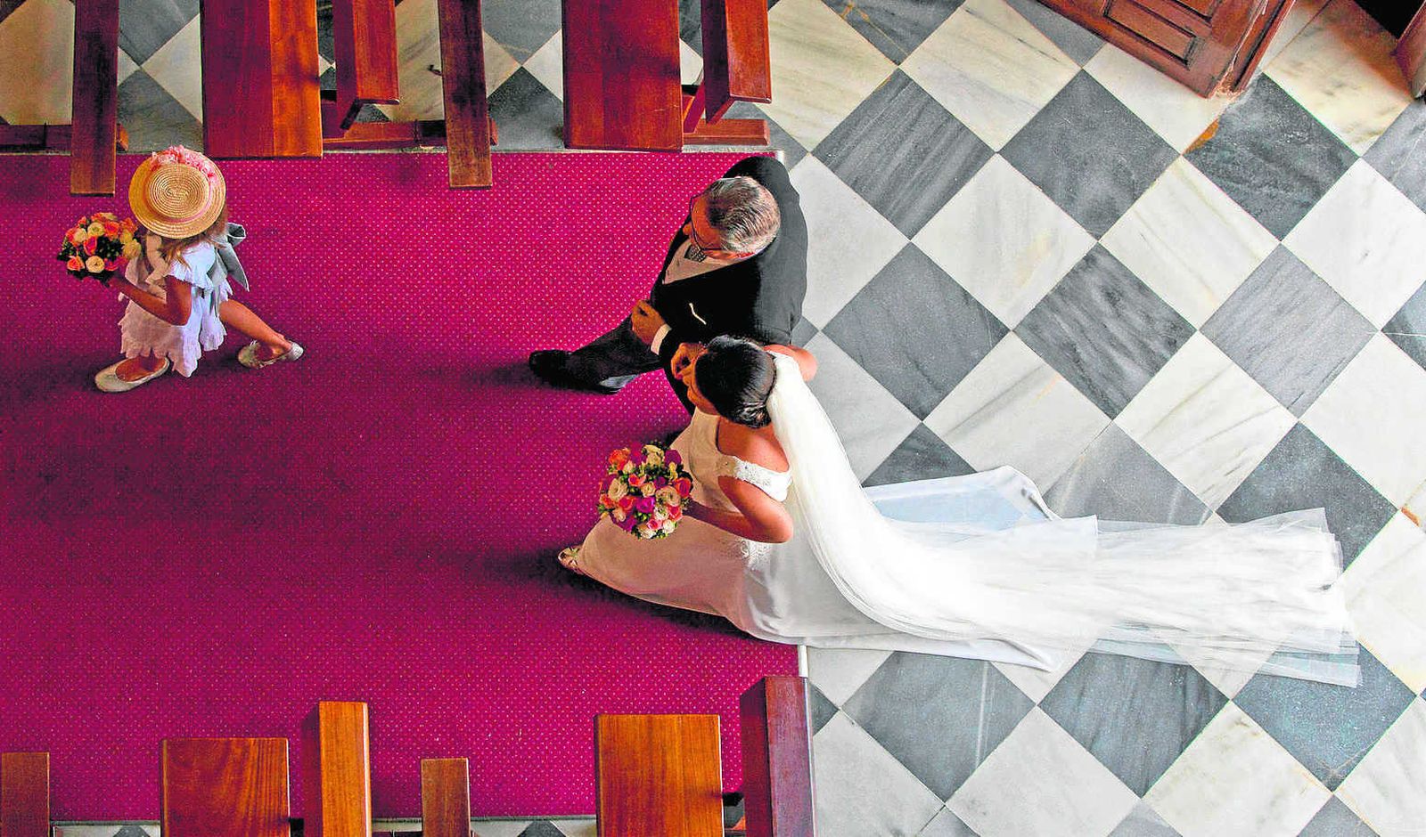 Una novia entra en la iglesia del brazo de su padrino y precedida por una niña de acompañante..