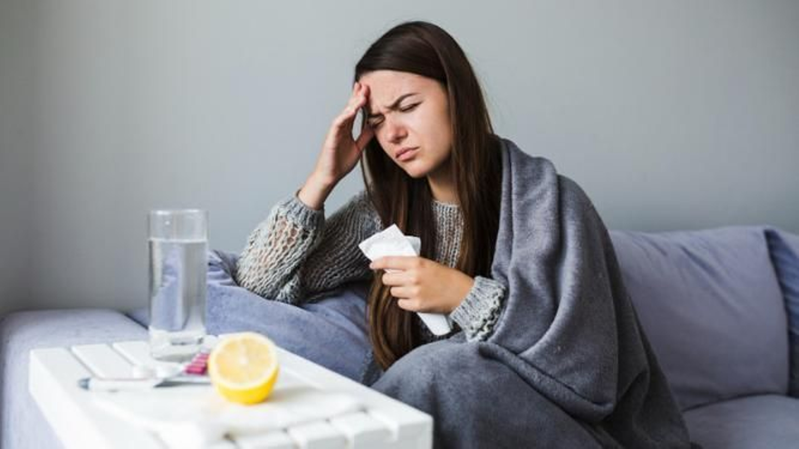 Mujer resfriada tomando medicamentos en el sofá.