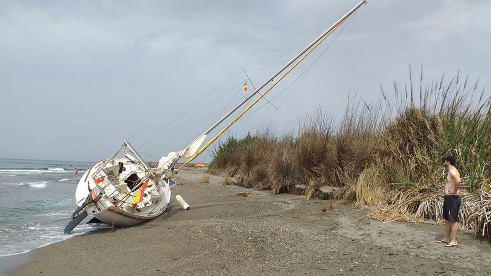 Un hombre mira el velero varado en Salobreña