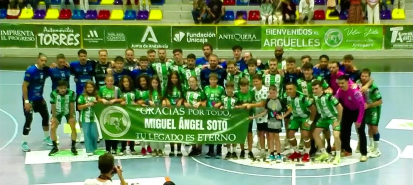 Los jugadores de ambos equipos posan con una pancarta en homenaje a Miguel Ángel Soto, entrenador de las bases de Los Dólmenes recientemente fallecido.