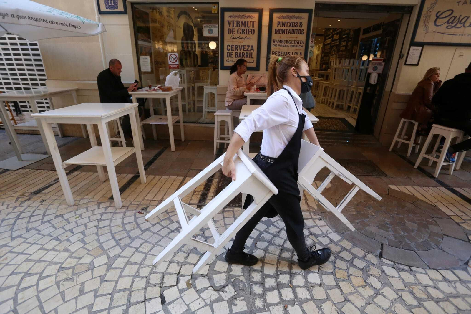 Una trabajadora recoge la terraza de un establecimiento de hostelería de Málaga capital.
