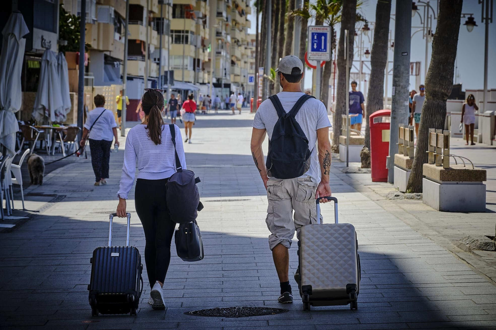 Dos turistas transitan por el Paseo Marítimo con sus maletas.