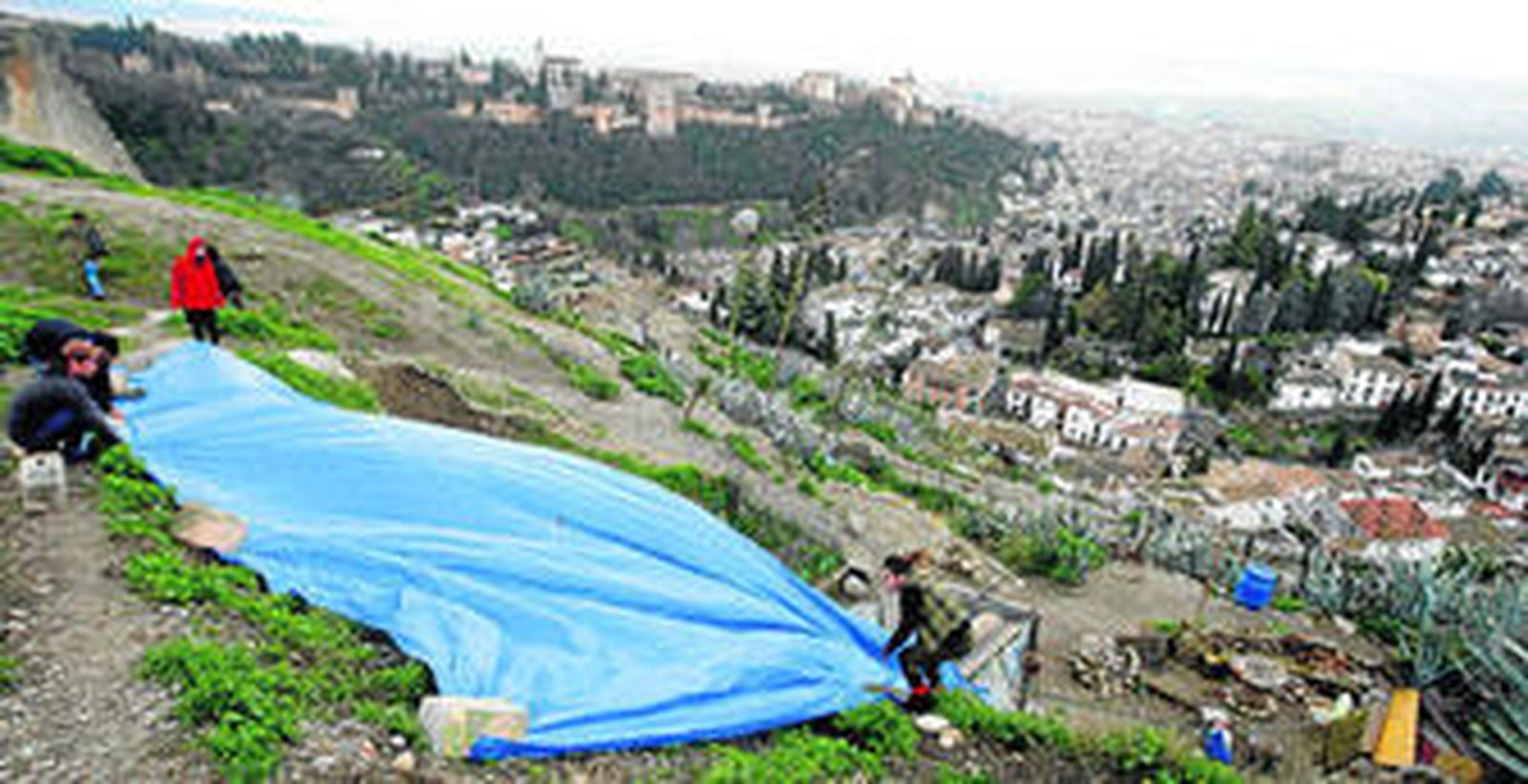Un grupo de jóvenes coloca una lona de plástico ayer en las cuevas del Sacromonte en Granada para filtrar el agua y la tierra que cae.