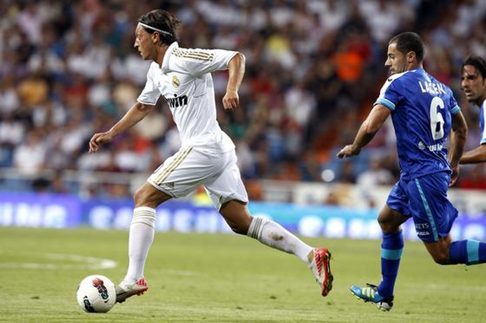 Özil conduce una pelota perseguido por un rival. / EFE