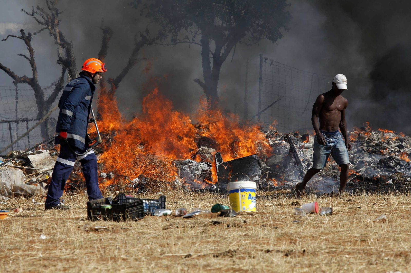Un agente contra incendios trabaja en un asentamiento chabolista ante la presencia de uno de sus habitantes.