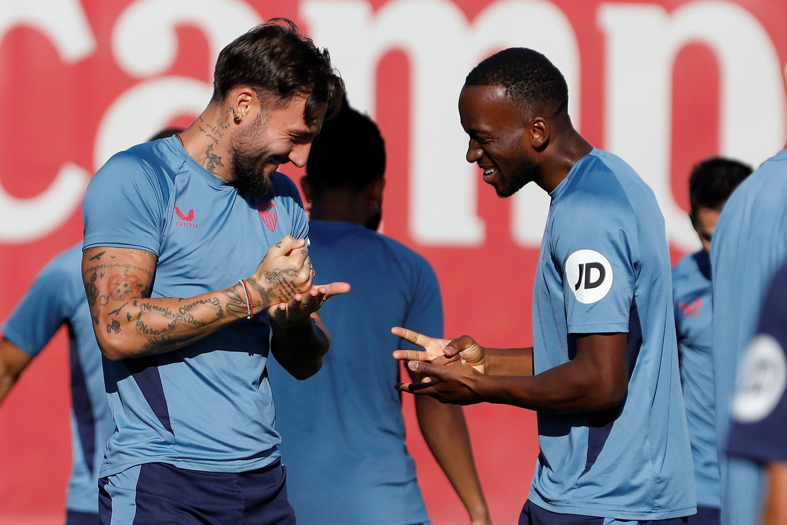 Gudelj y Lukébakio realizan un sorteo entre bromas en el entrenamiento del Sevilla.
