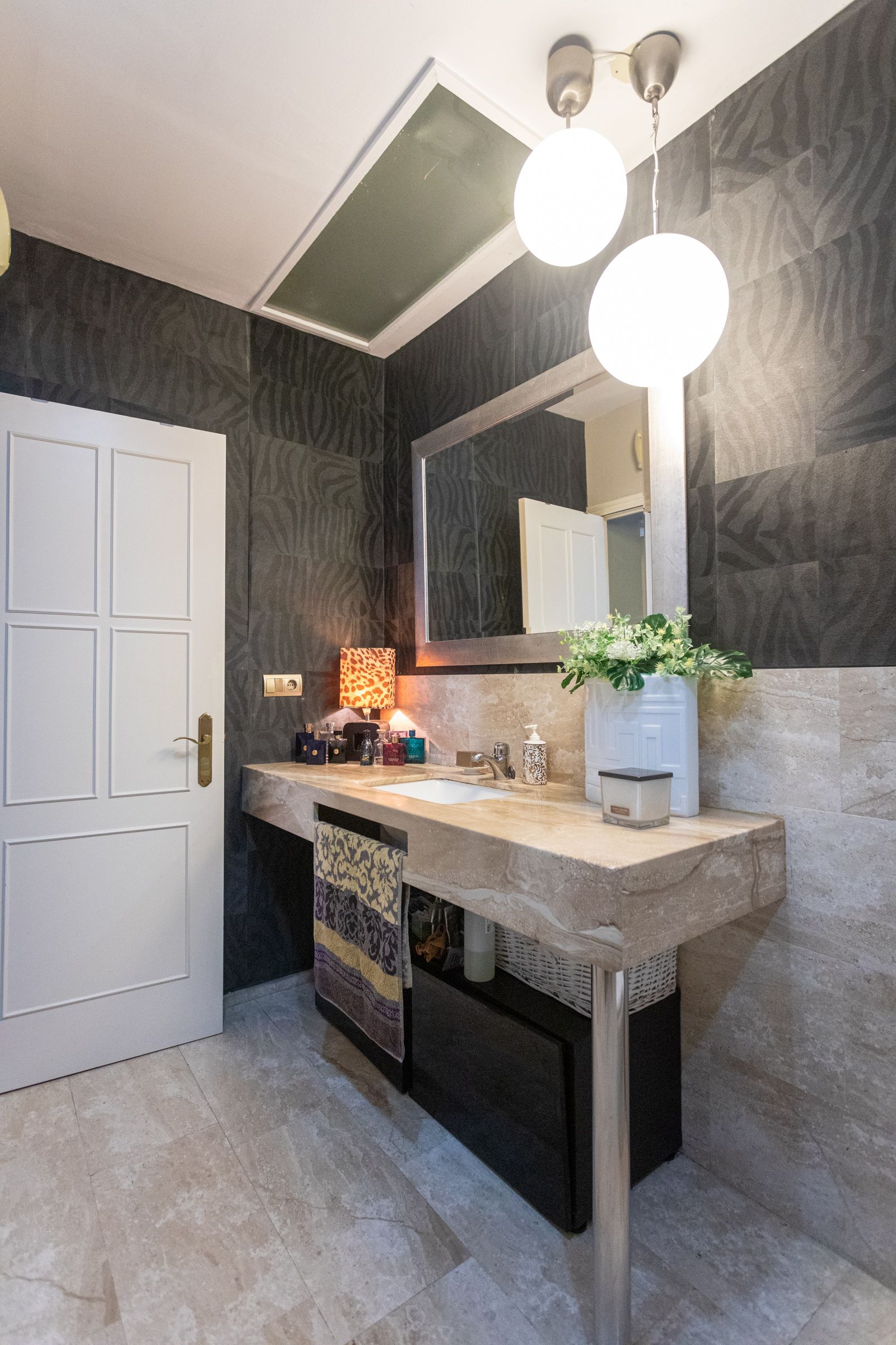 Baño.  Sus paredes están cubiertas por un papel negro de ‘animal print’. Lavabo y espejo se iluminan con dos globos de los años 70.