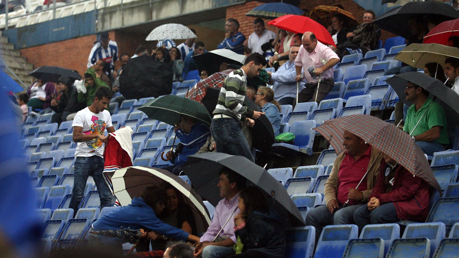 Aficionados se refugian de la lluvia bajo sus paraguas durante el Recre-Lugo.