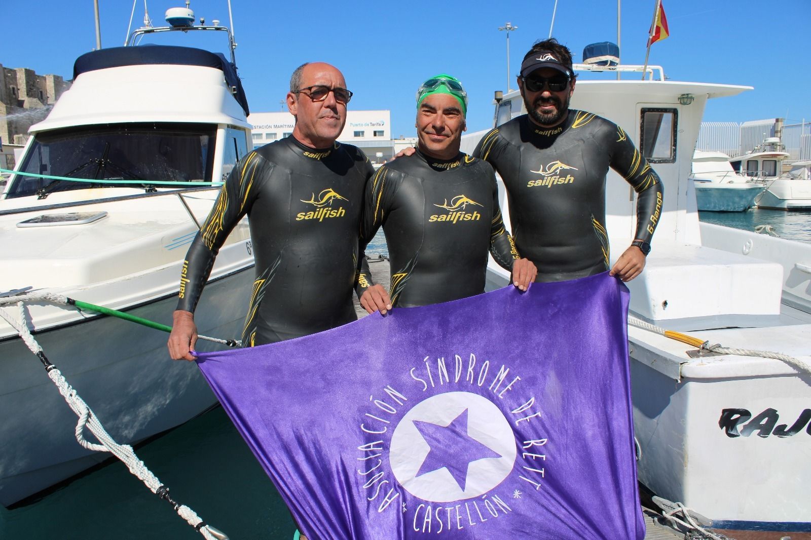 Los tres nadadores, con la bandera de su asociación, en el puerto de Tarifa