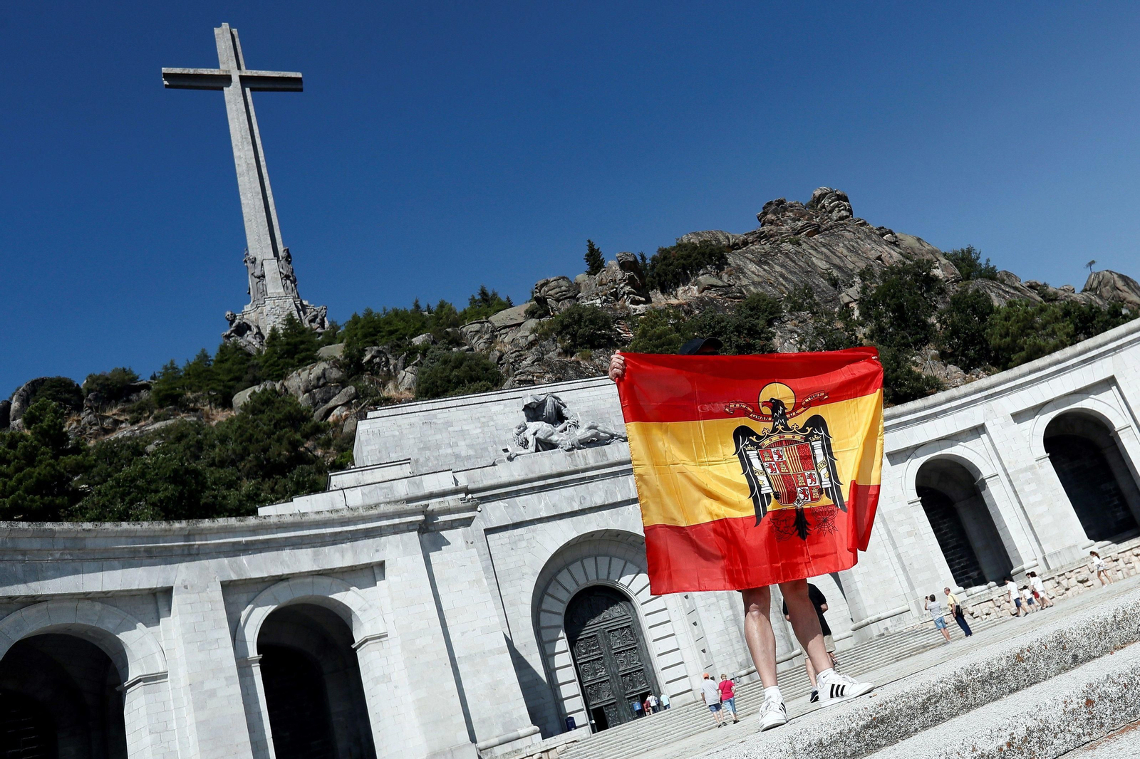 Una persona despliega una bandera anticonstitucional en la esplanada del Valle de los Caídos.