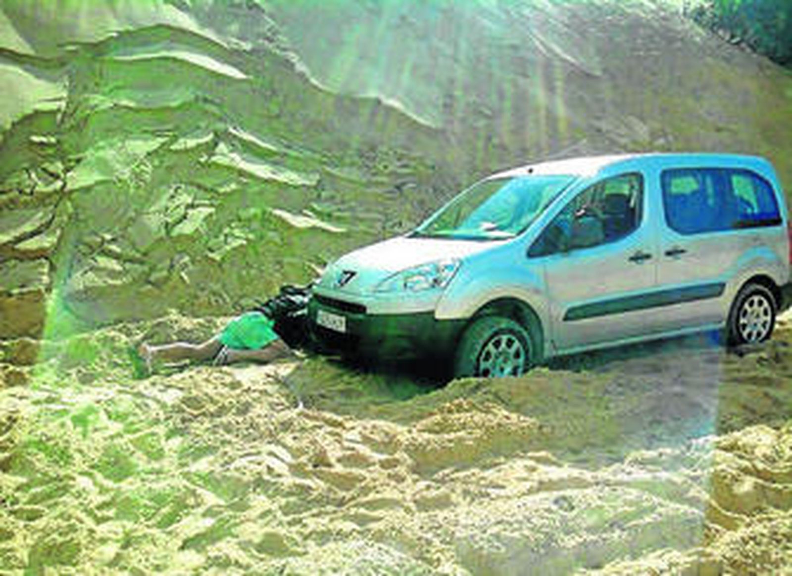 Una persona, tirada junto a la parte delantera de la furgoneta, trata de retirar la arena de la duna, ayer.