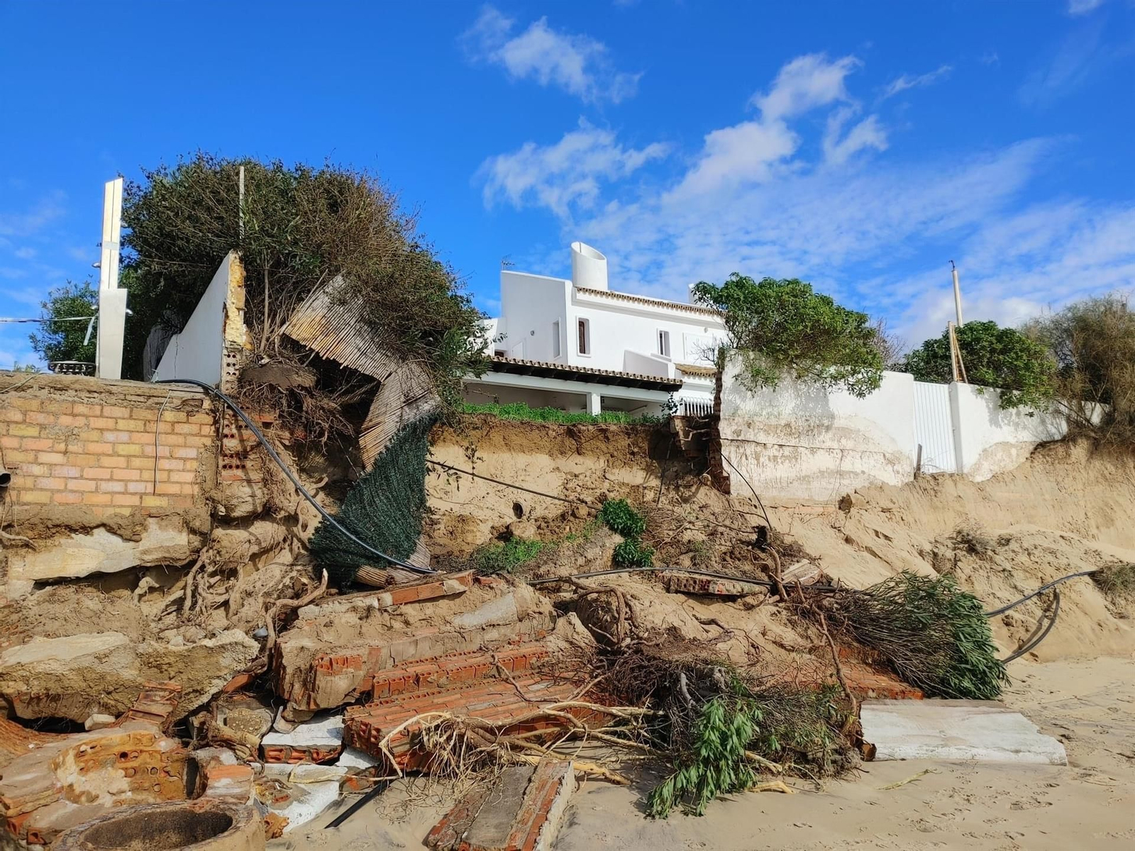 Imagen del estado de la playa de El Portil  este fin de semana tras el temporal y de la caída de un muro cercano a una vivienda.