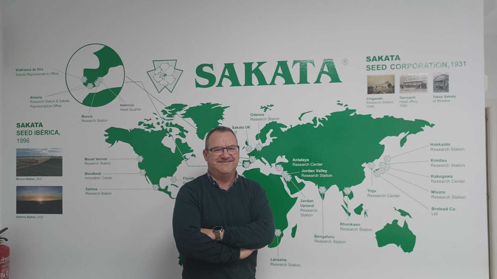 Francisco Javier posa en las oficinas de Sakata, delante de un gran mapa mundial.