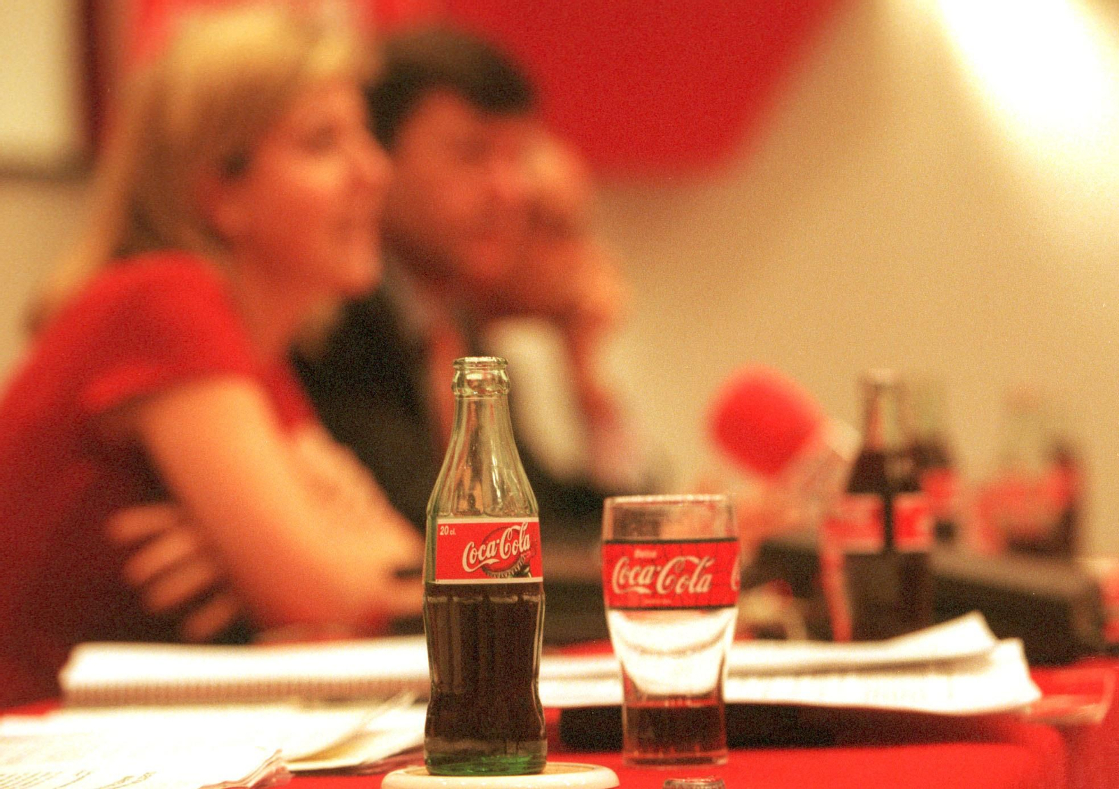 Una botella de Coca Cola junto a folios en blanco.