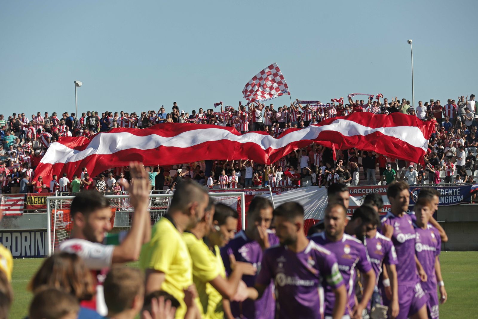 Los jugadores del Algeciras y el Real Jaén se saludan con el fondo sur lleno de colorido.