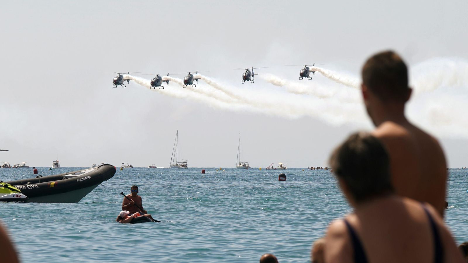 Bañistas contemplan helicópteros en una exhibición del Festival Aéreo de Torre del Mar.