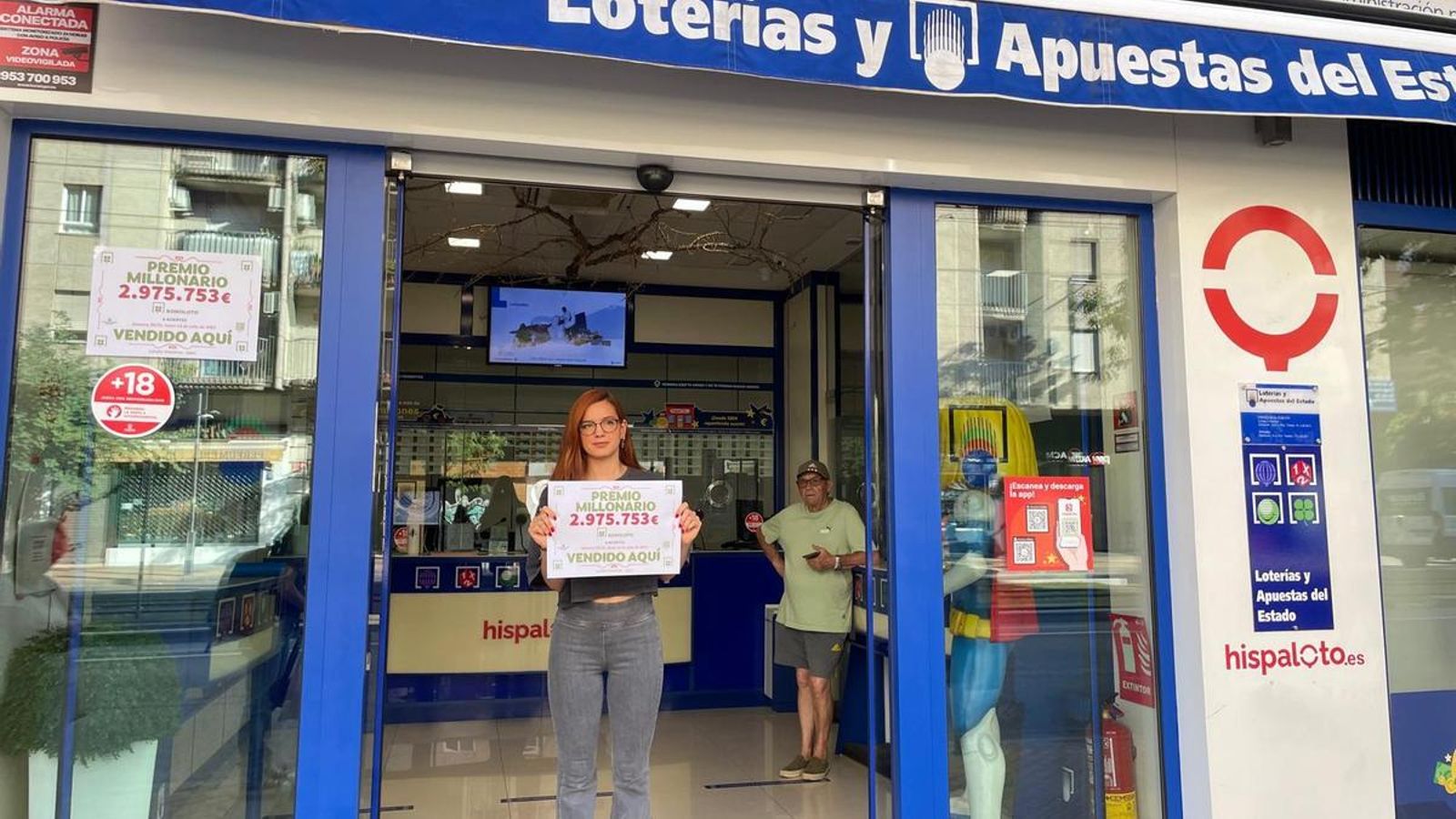 Trabajadora de la administración de lotería con el cartel del premio de la bonoloto.