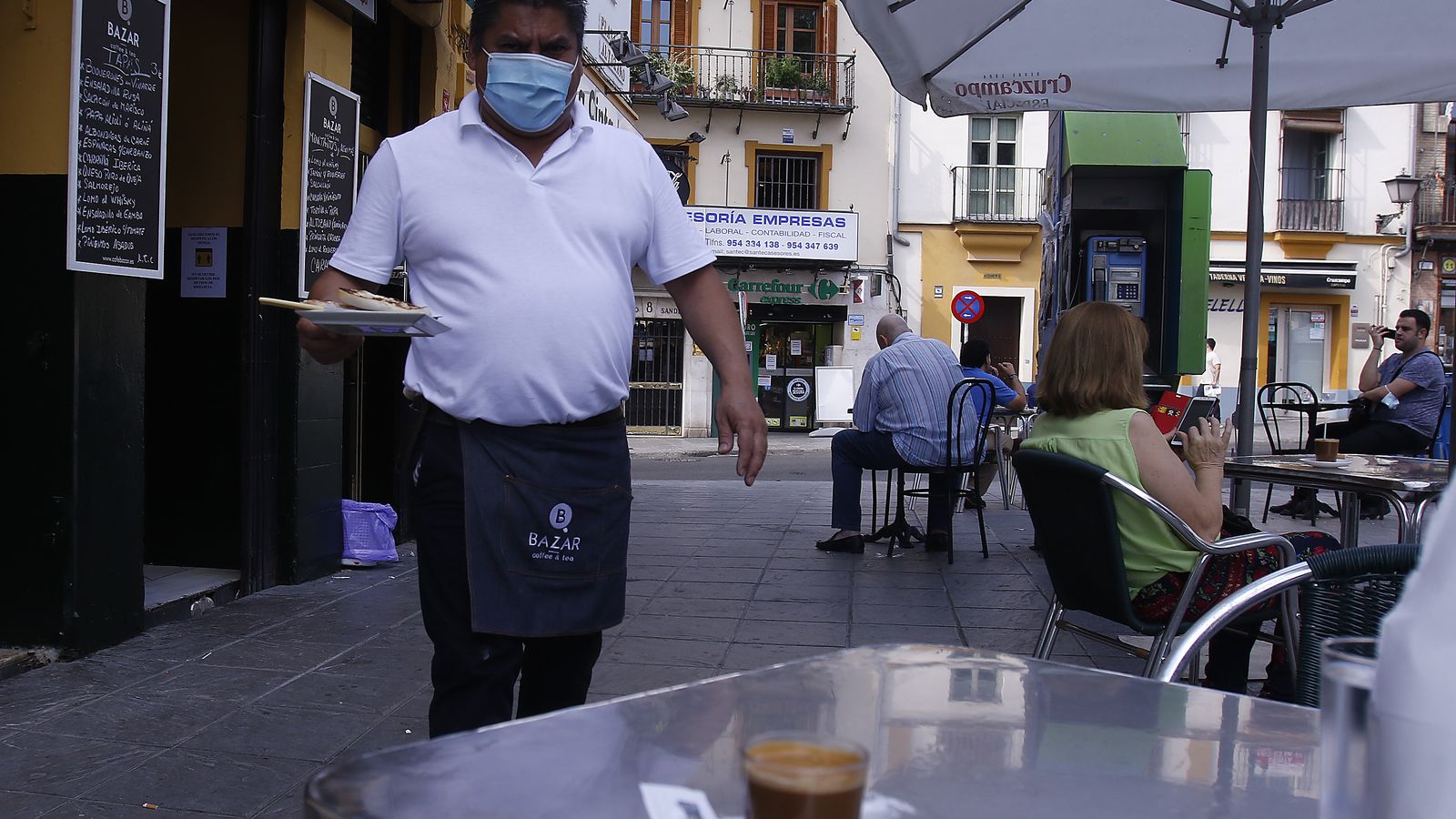 Un camarero con mascarilla atiende la mesa de un bar.