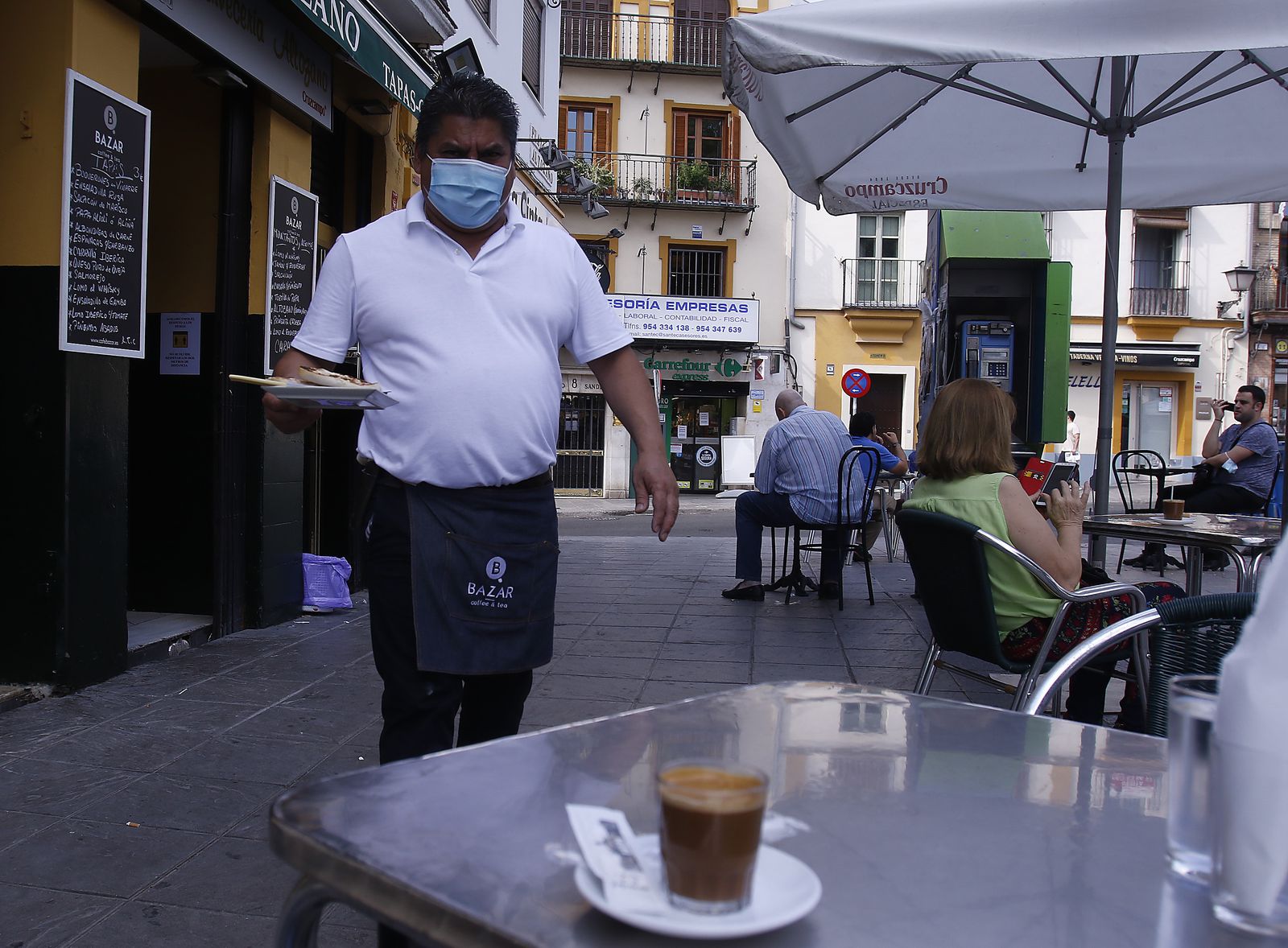 Un camarero con mascarilla atiende la mesa de un bar.