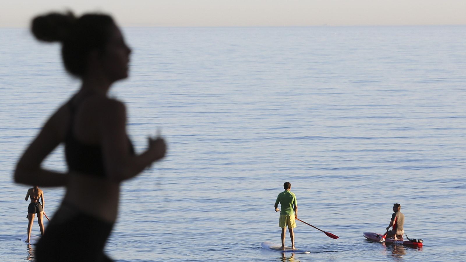 Una corredora y varias personas haciendo paddle surf.