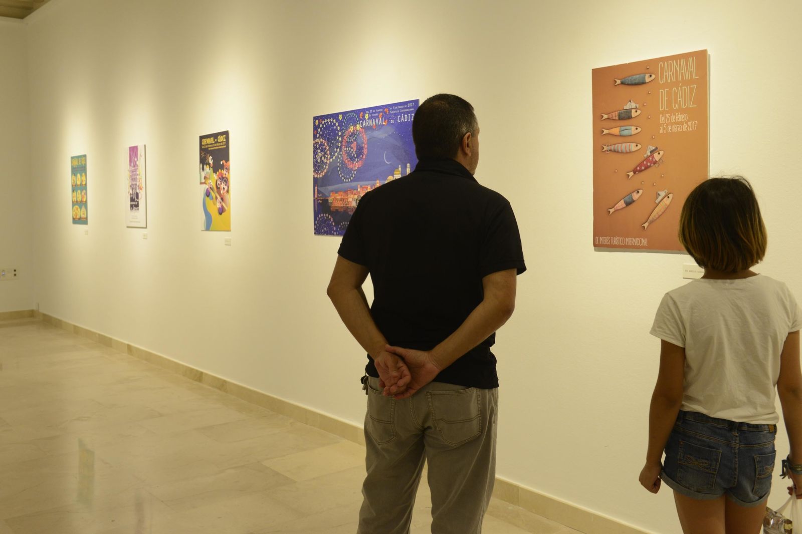 Dos personas observan algunas de las obras expuestas para la elección del cartel del Carnaval 2017.