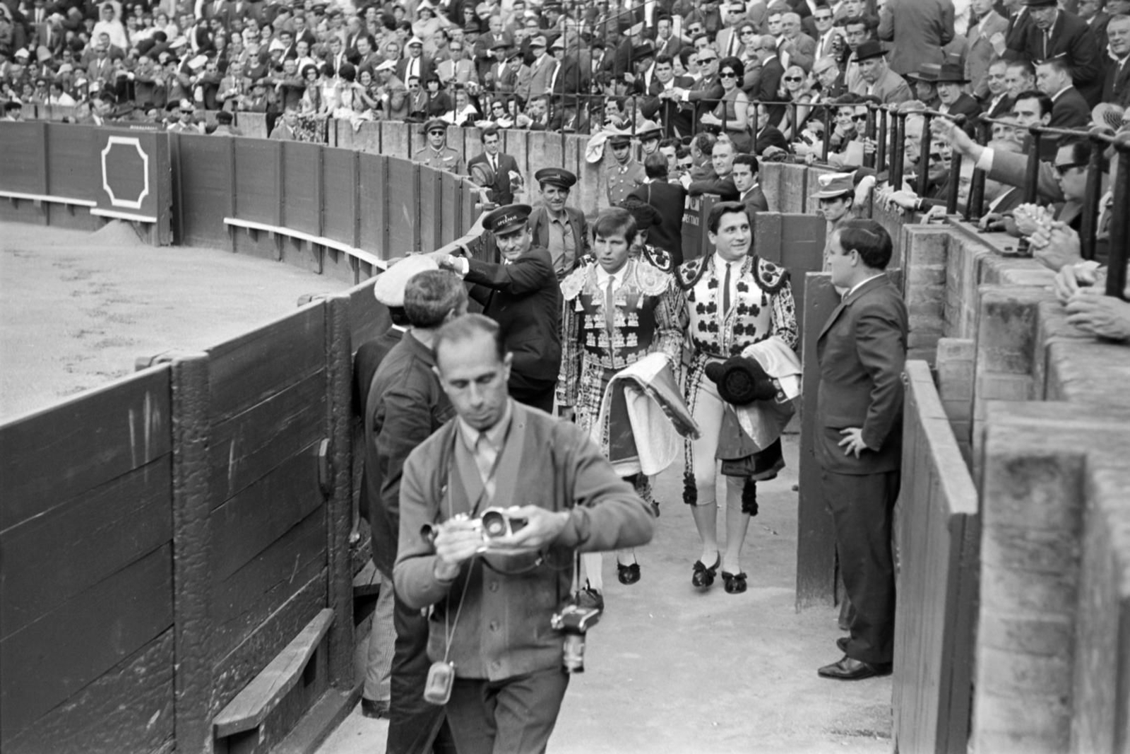 Capote de paseo y montera en la mano, Manuel Benítez llega por el callejón en compañía de un sonriente Paquito Ruiz, su peón de confianza.