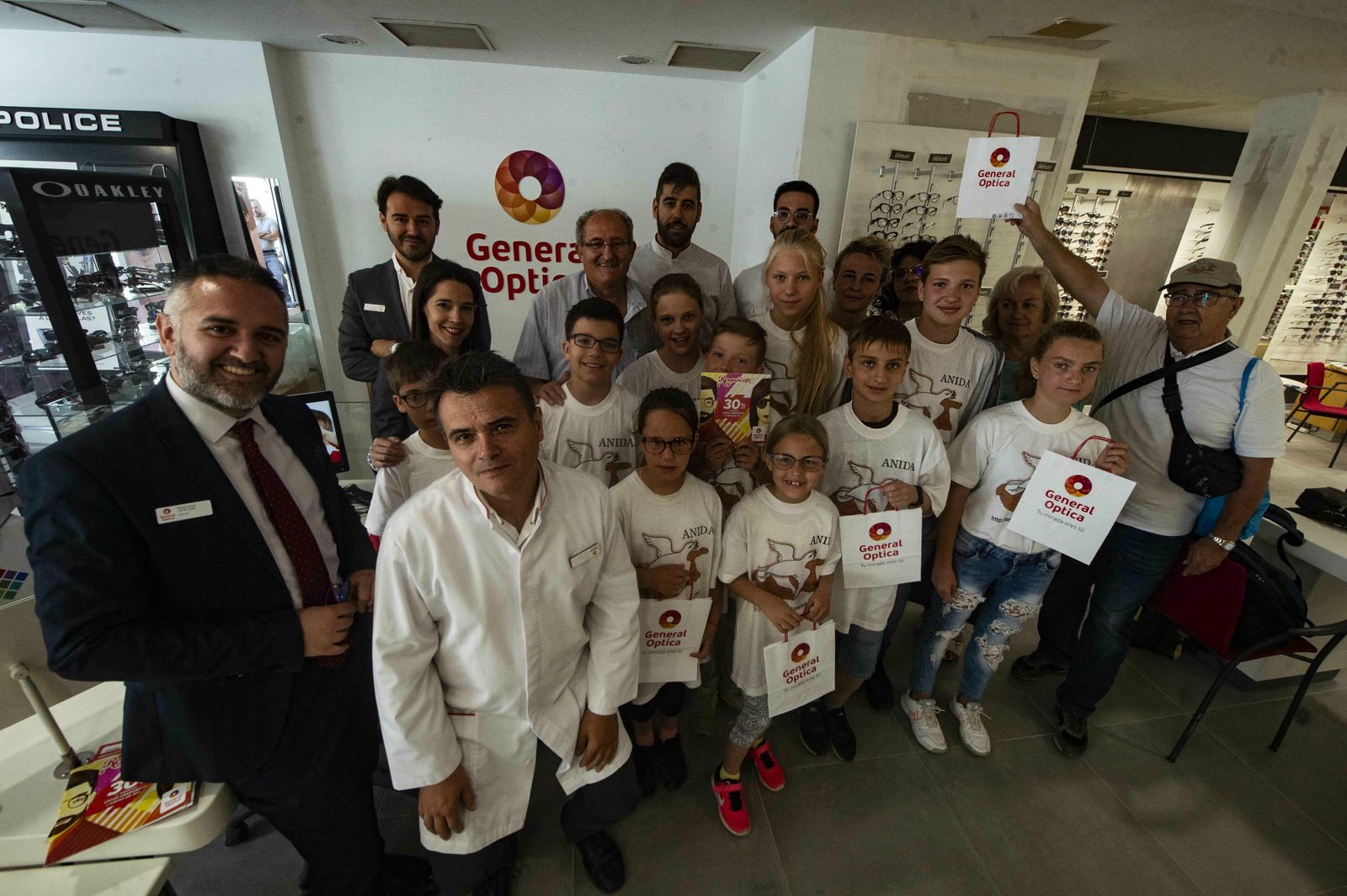 El grupo de niños y Anida posan con el equipo de General Óptica.