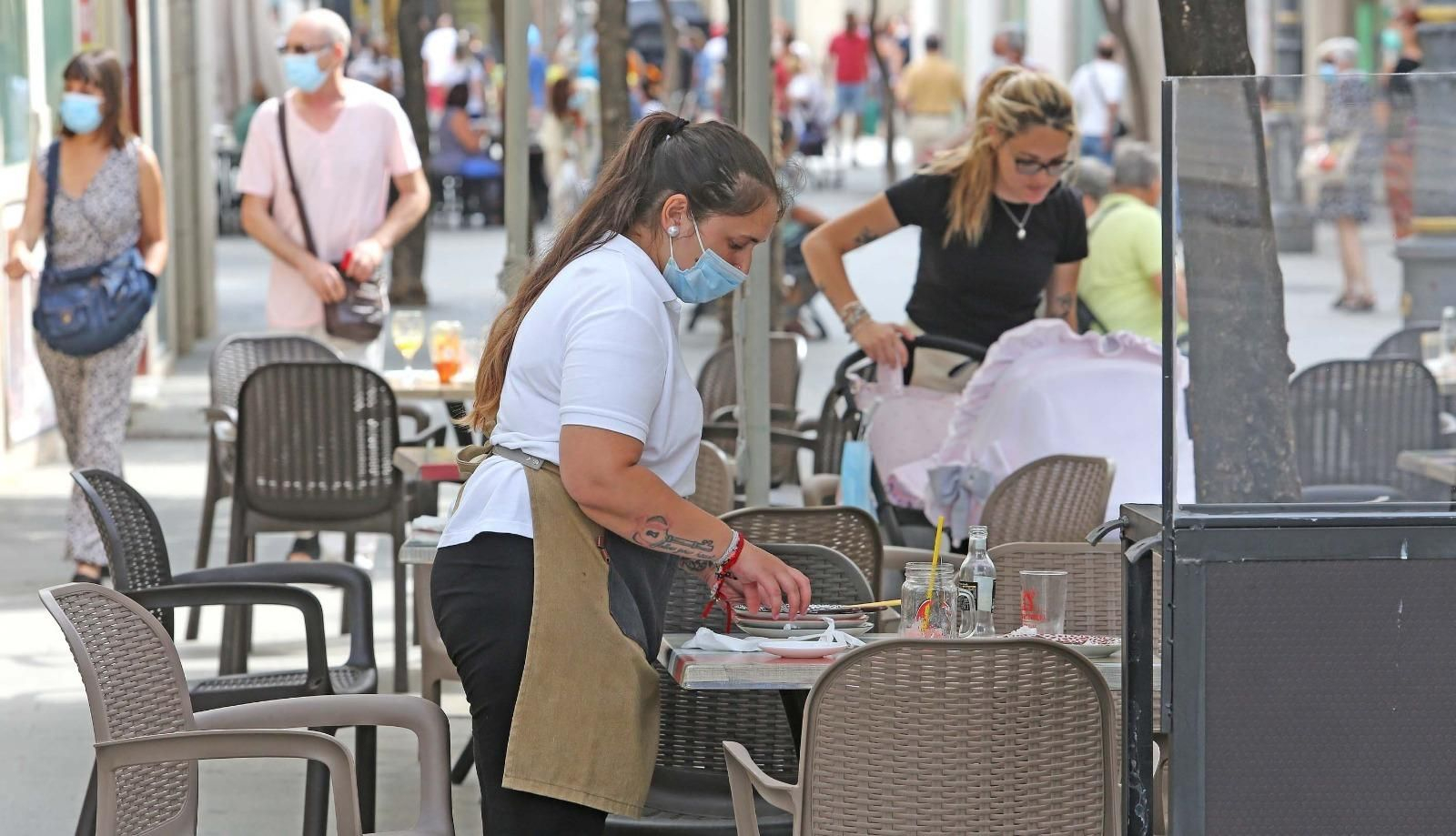 Una camarera recoge la mesa en la terraza de un bar en la calle Larga Una camarera recoge la mesa en la terraza de un bar en la calle Larga