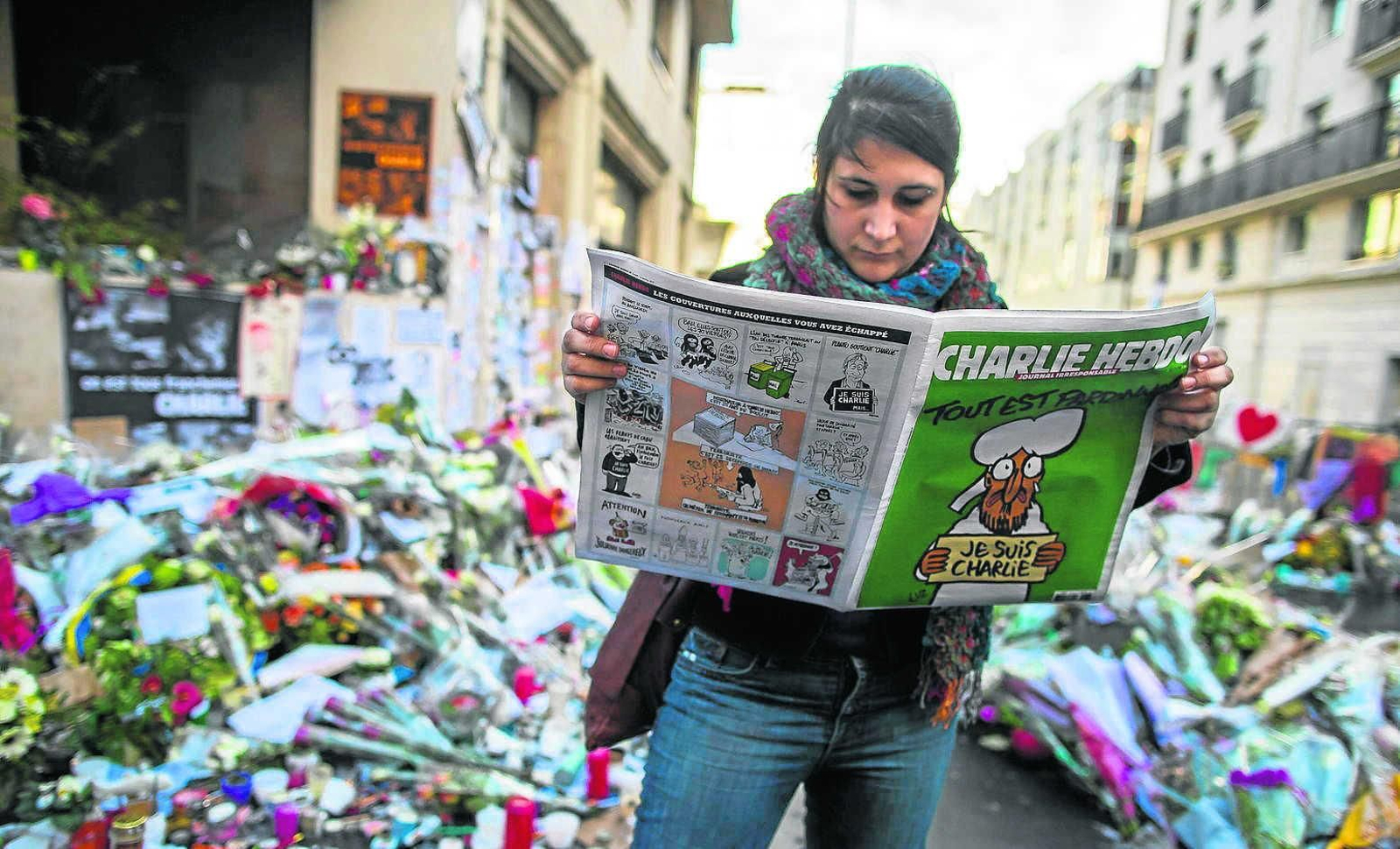 Una mujer lee el semanario 'Charlie Hebdo' ante el memorial levantado en París en enero de 2015.