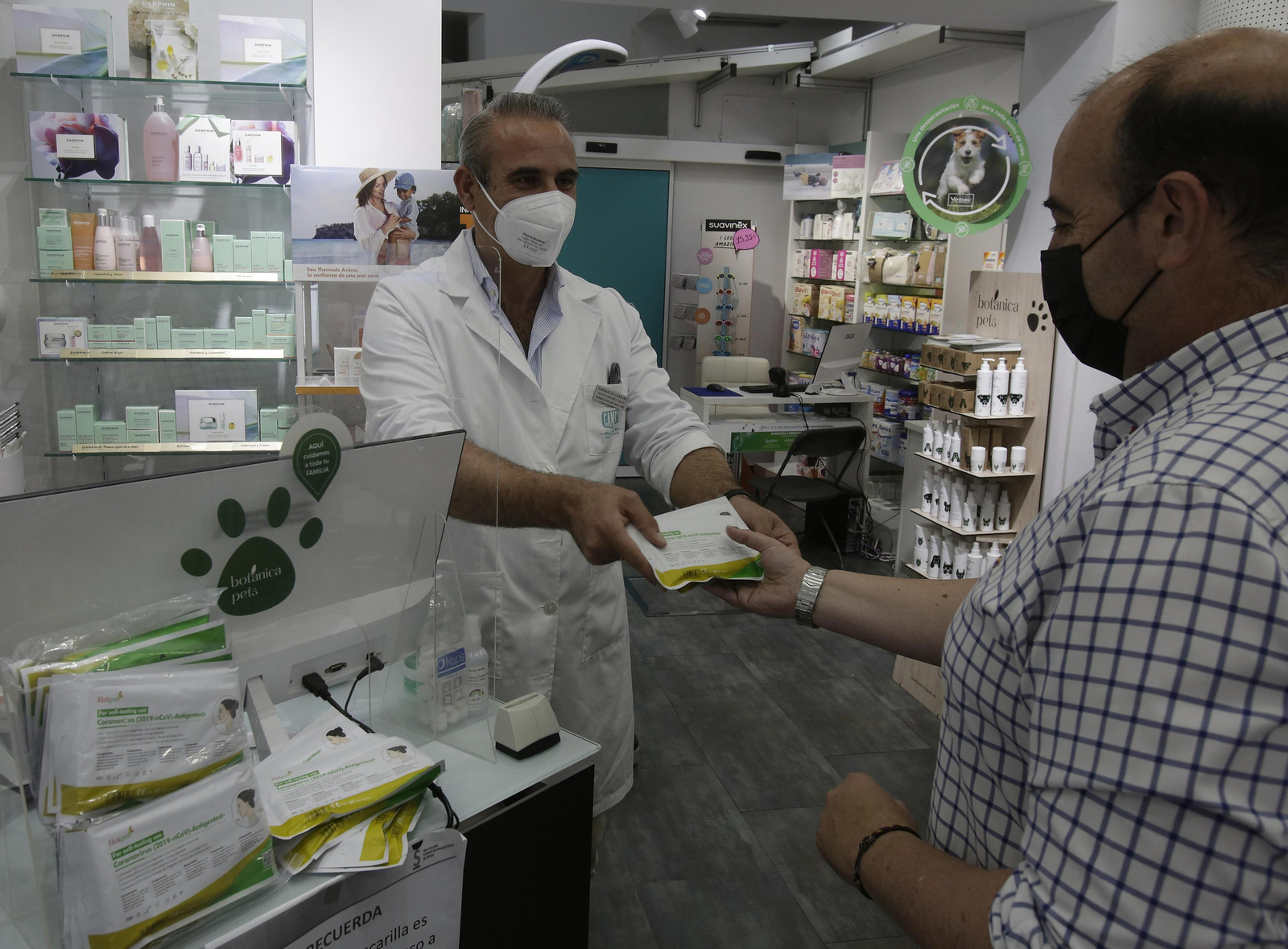 El farmacéutico Julio Cansino entrega un test de antígenos a un cliente en su farmacia en Castilleja de la Cuesta.