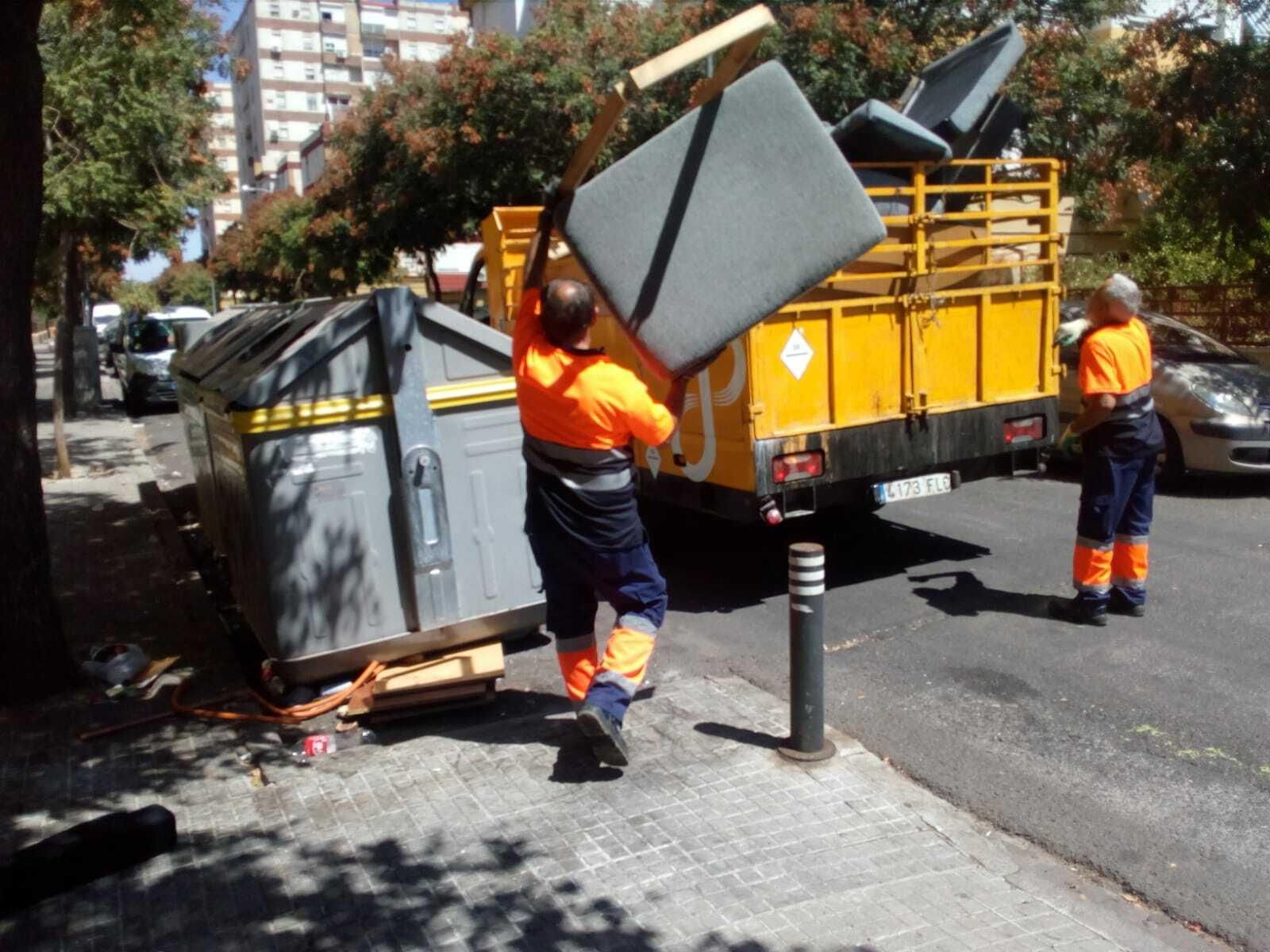 Dos operarios del servicio de limpieza de Lipasam recogen arrojan un mueble al camión.