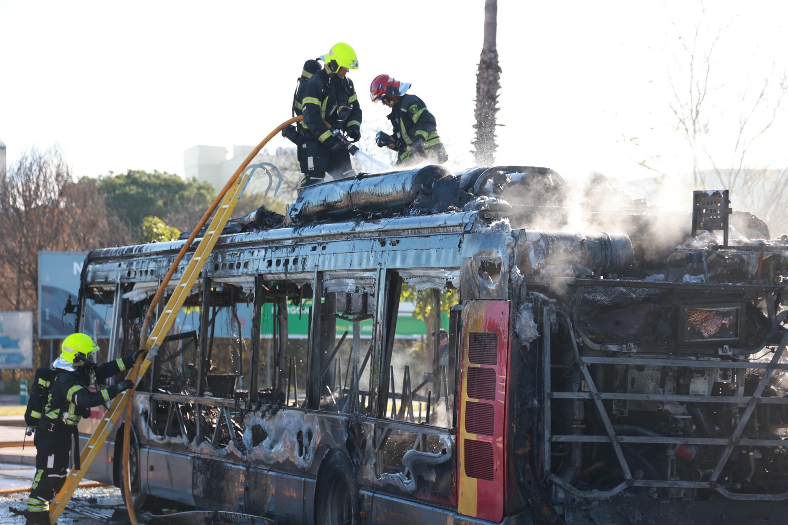 Los Bomberos sobre el autobús quemado por completo.