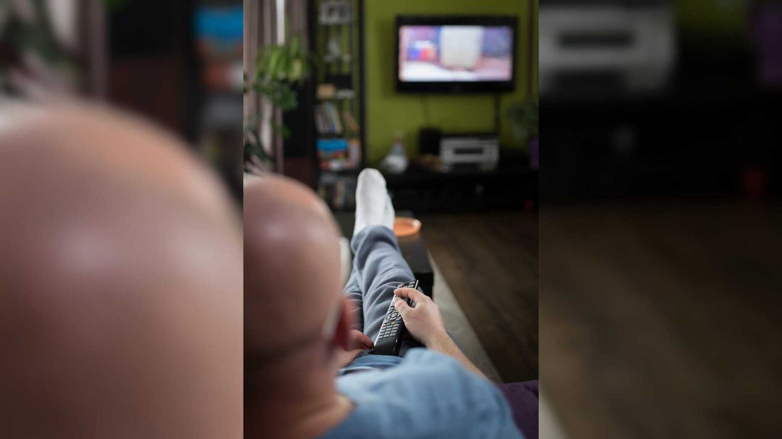 Un joven ve la televisión, mando en mano, desde su sofá.