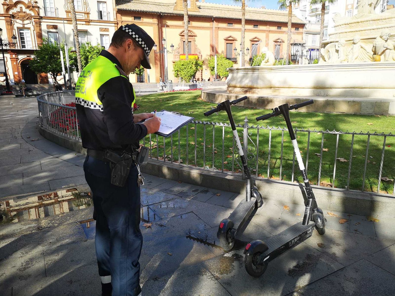 Un agente multa el aparcamiento irregular de patinetes eléctricos en una zona peatonal, como la Puerta de Jerez.