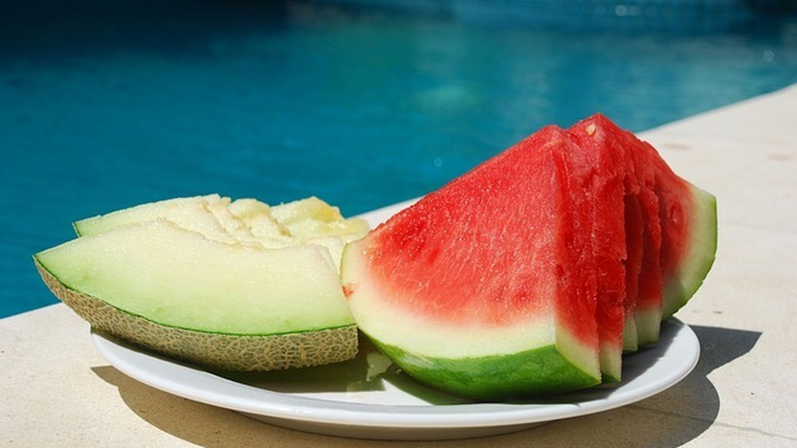 Varias piezas de melón y sandía junto a una piscina