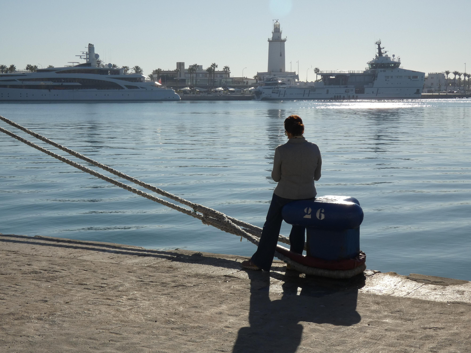 Una turista sentada sobre un noray ocupado por dos estachas en el muelle número dos. Una turista sentada sobre un noray ocupado por dos estachas en el muelle número dos.