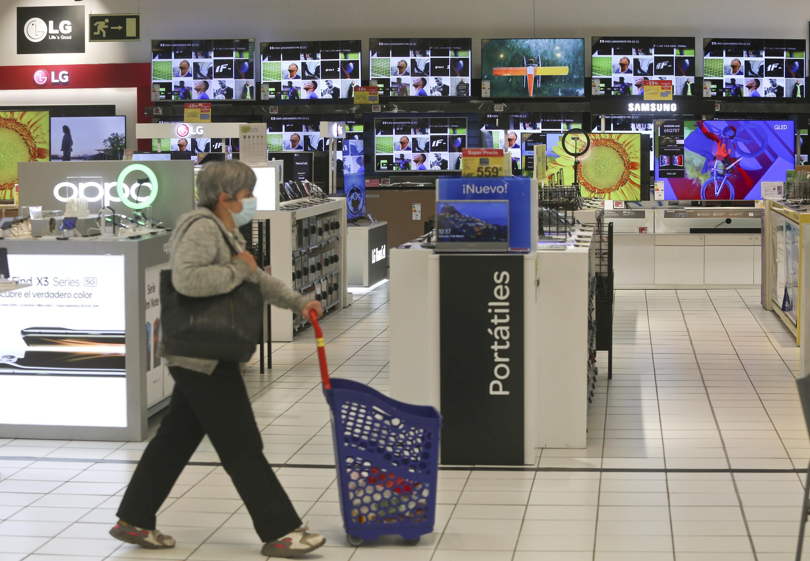 Mujer pasando por el pasillo de las televisiones en un supermercado. Mujer pasando por el pasillo de las televisiones en un supermercado.